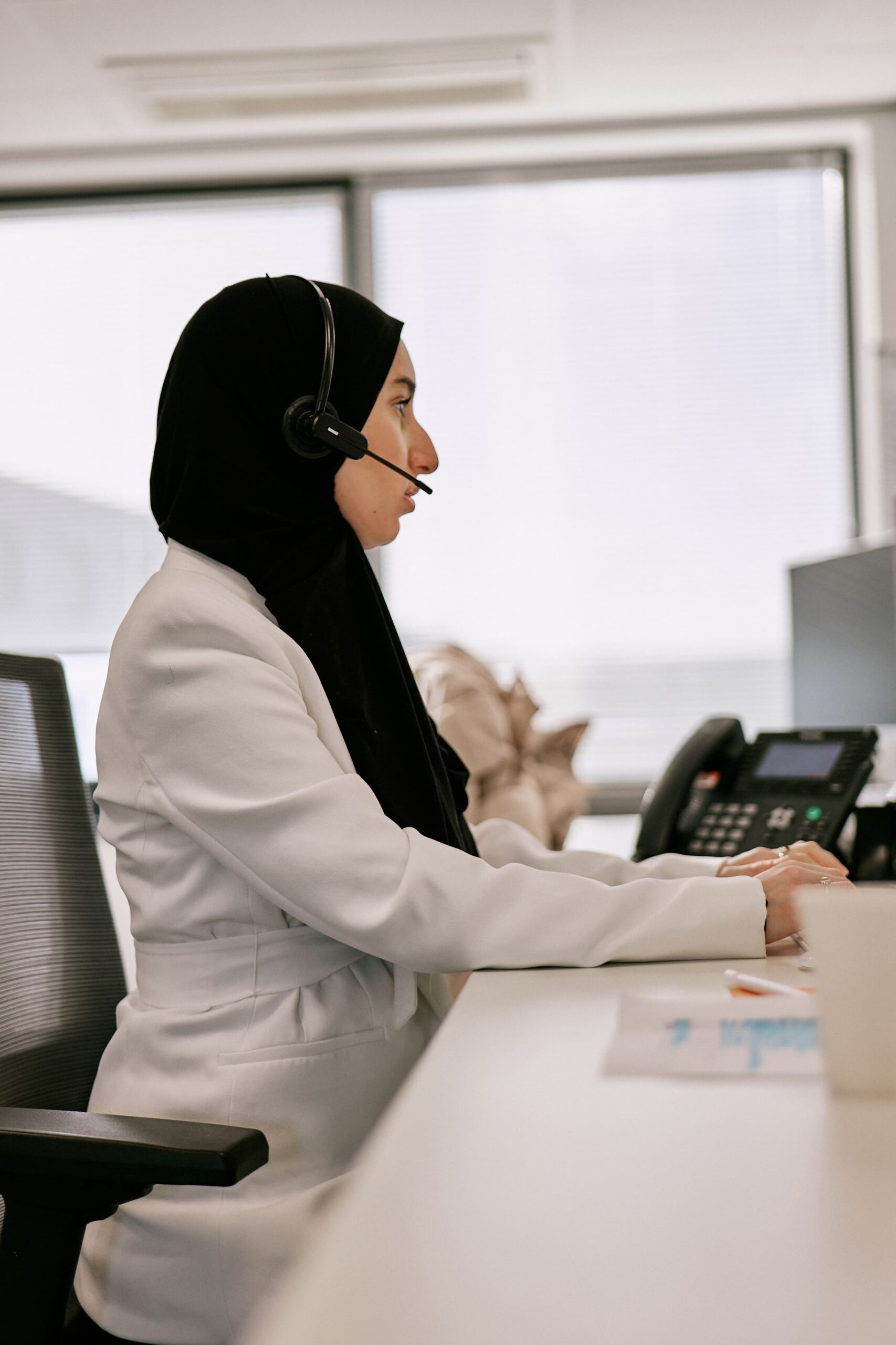 Vrouw met een hijab aan het werk in het kantoor van Trias Legal, terwijl ze een headset draagt en aan het typen is op een computer.